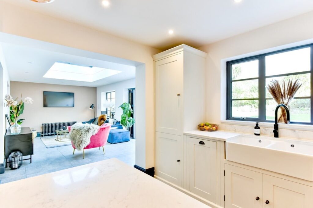 Image of a kitchen extension with skylights and neutral colours, featuring a spacious open plan design with a large island, modern appliances and dining area. The skylights provide ample natural light, while the neutral colour palette creates a sleek and contemporary look. This image is featured on a blog post about open plan living ideas.