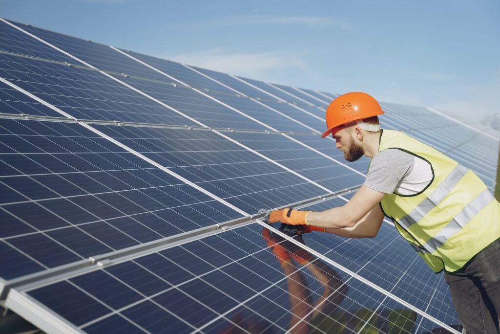 A solar panel installer is installing solar panels on a homeowner's roof. The installer is standing on the roof, and there are solar panels nearby.