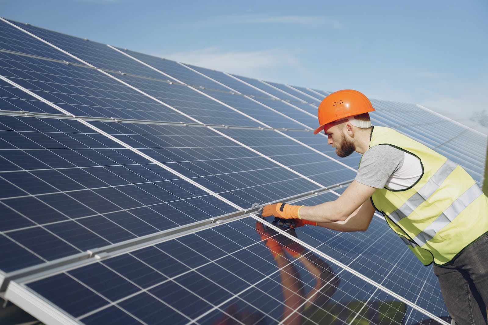 A solar panel installer is installing solar panels on a homeowner's roof. The installer is standing on the roof, and there are solar panels nearby.